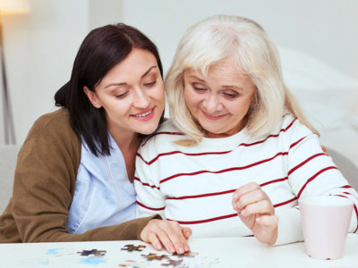 caregiver helping elderly woman to complete jigsaw puzzle